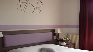 A hotel room with a large bed, a headboard, two bedside lamps, a nightstand, a vase with flowers, and a red curtain.