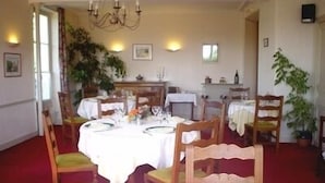 Ein Esszimmer mit einer Kronleuchter, mehreren gedeckten Tischen, Holzsesseln und Topfpflanzen.