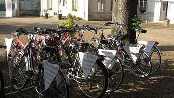 Bicycles parked outside a building with a tree and a gate in the background.