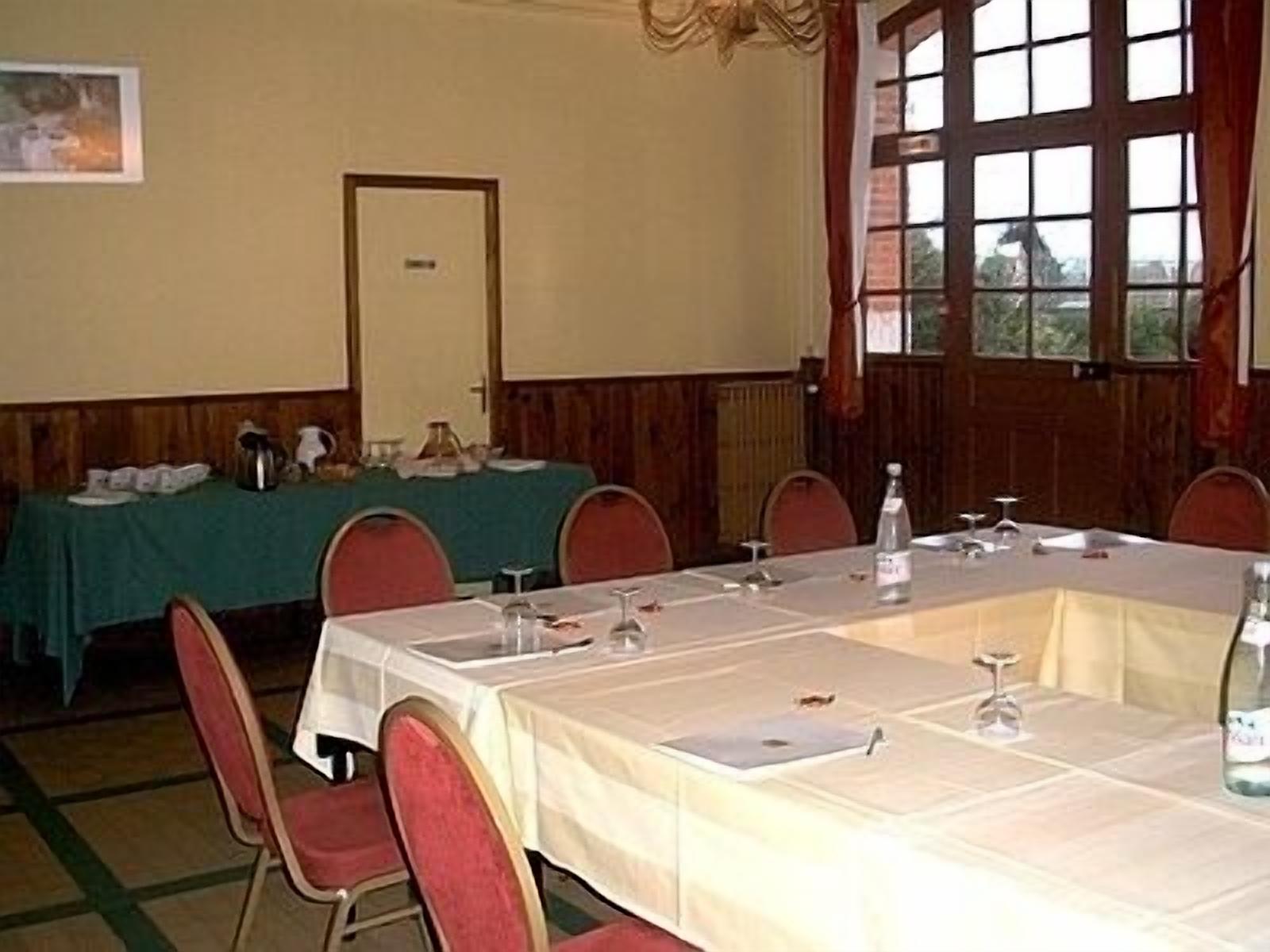 A conference room with a long table, red chairs, and a green tablecloth. There is a window with curtains and a door in the background.