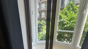 A room with a sliding glass door leading to a balcony with a view of a building and greenery. - Hostal Balmes Centro (Barcelona)
