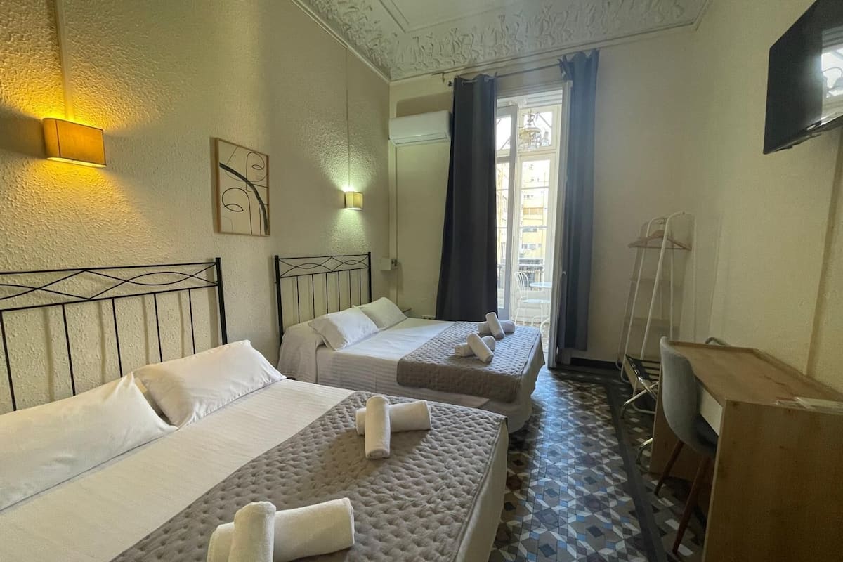 Habitación de hotel con dos camas, un escritorio y una silla. Hay toallas sobre las camas y un cuadro en la pared.