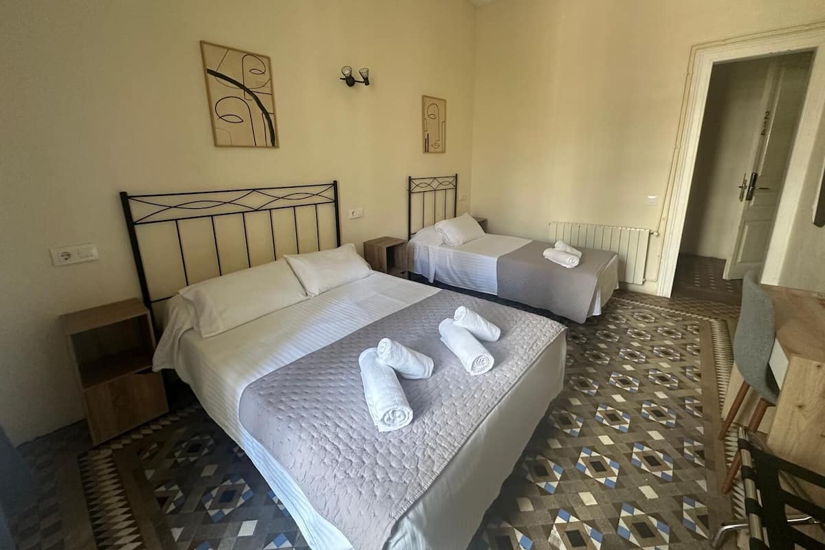 Habitación de hotel con dos camas, cada una con una toalla doblada con cuidado, una mesita de noche y una lámpara de pared.
