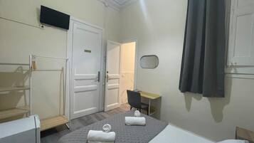 Habitación de hotel con cama, escritorio, silla, televisión y espejo.