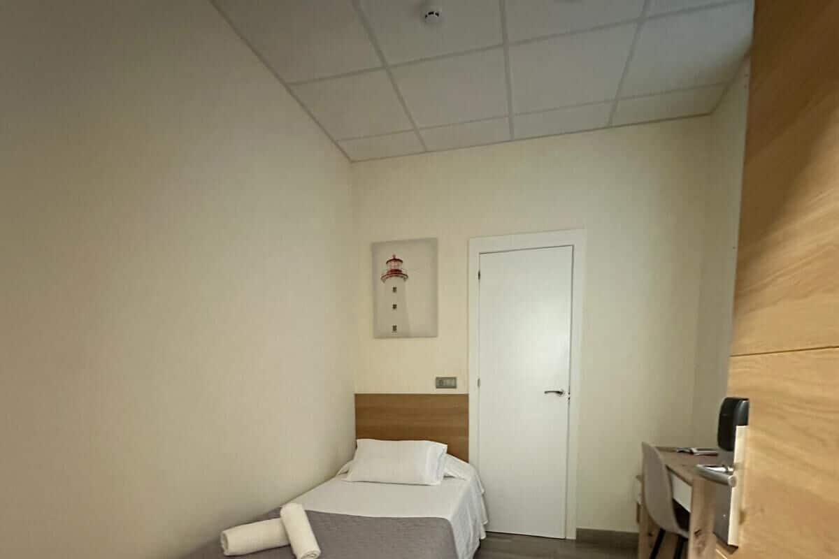 Una habitación de hotel pequeña y estrecha con una cama individual, un escritorio y una kitchenette.