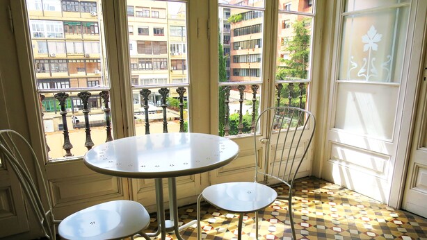 A room with a round table and two chairs, large windows with a view of buildings, and a patterned floor. - Hostal Balmes Centro (Barcelona)