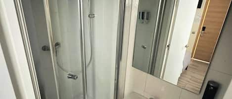 Ein modernes Badezimmer mit einer Duschkabine, einem Standwaschbecken und einem Spiegel darüber.