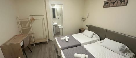 Habitación de hotel con dos camas, un escritorio, una silla, un armario y un baño visible a través de una puerta abierta.