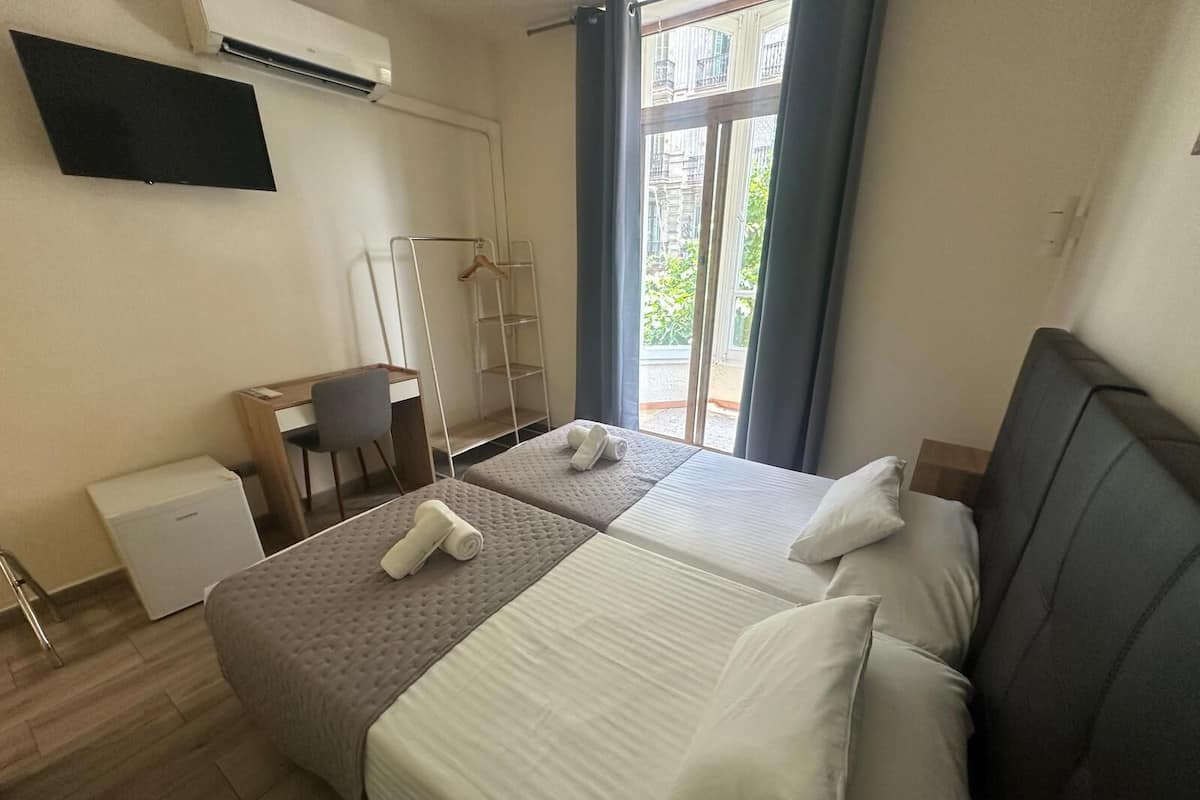 Habitación de hotel con dos camas, un escritorio, una silla, un armario y vistas a zonas verdes por la ventana.