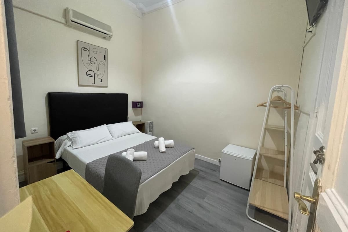 Habitación de hotel con cama, mesita de noche, pequeño escritorio, silla, armario, espejo y calefactor.
