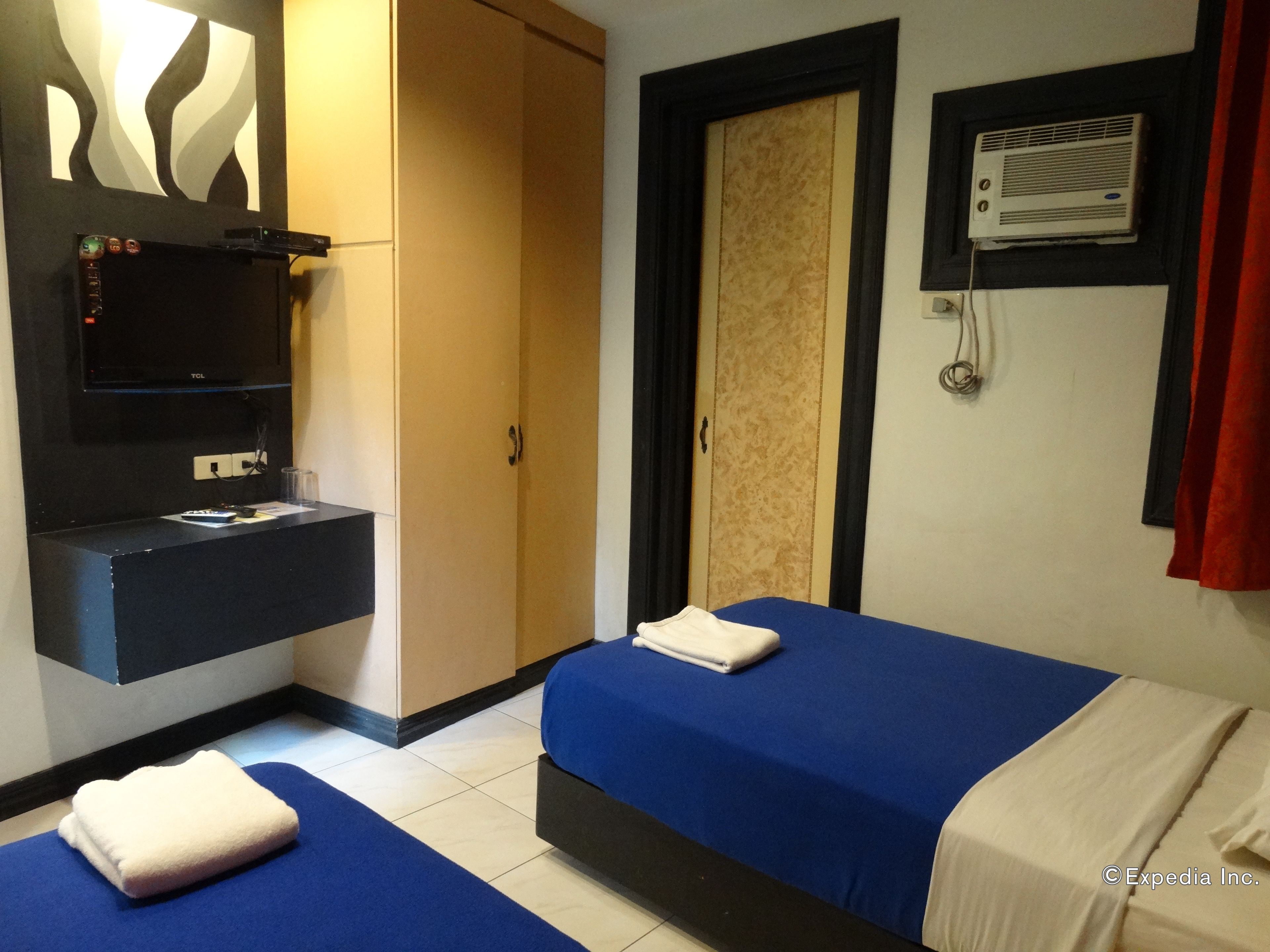 A hotel room with two beds, a minibar, a mirror, a wardrobe, and a wall-mounted air conditioning unit.