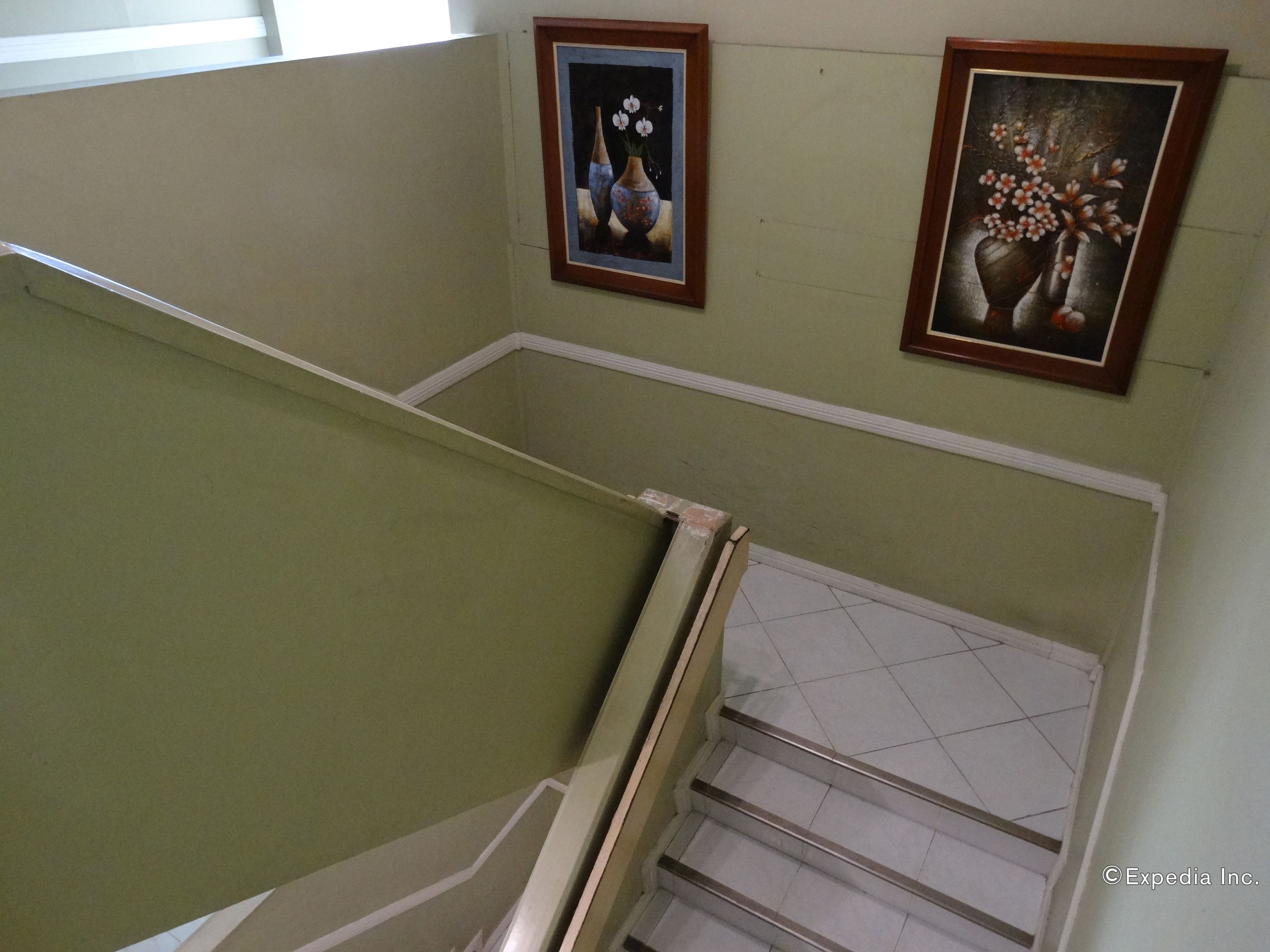 A staircase with a handrail, a tiled floor, and two framed paintings on the wall.