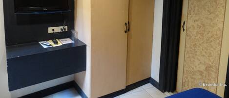 A room with a flat-screen TV mounted on a black wall, a small table with a remote control, and a beige wardrobe with a mirror.