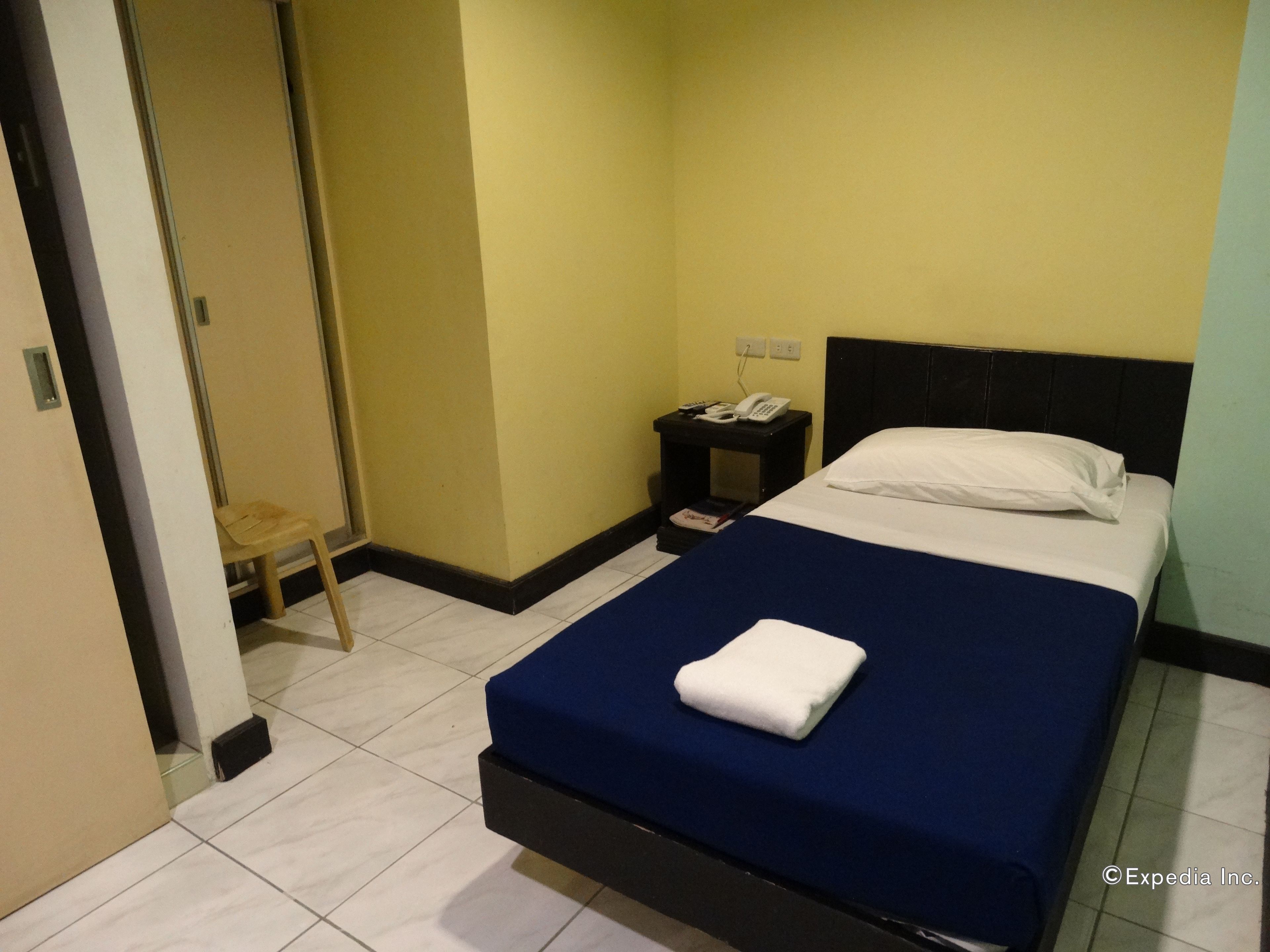 A hotel room with a bed, a nightstand with a phone, and a small stool.