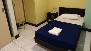 A hotel room with a bed, a nightstand with a phone, and a small stool.