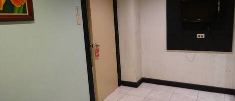 A room with a blue massage table, a door with a red tag, a framed flower on the wall, and a black TV mounted on the wall.