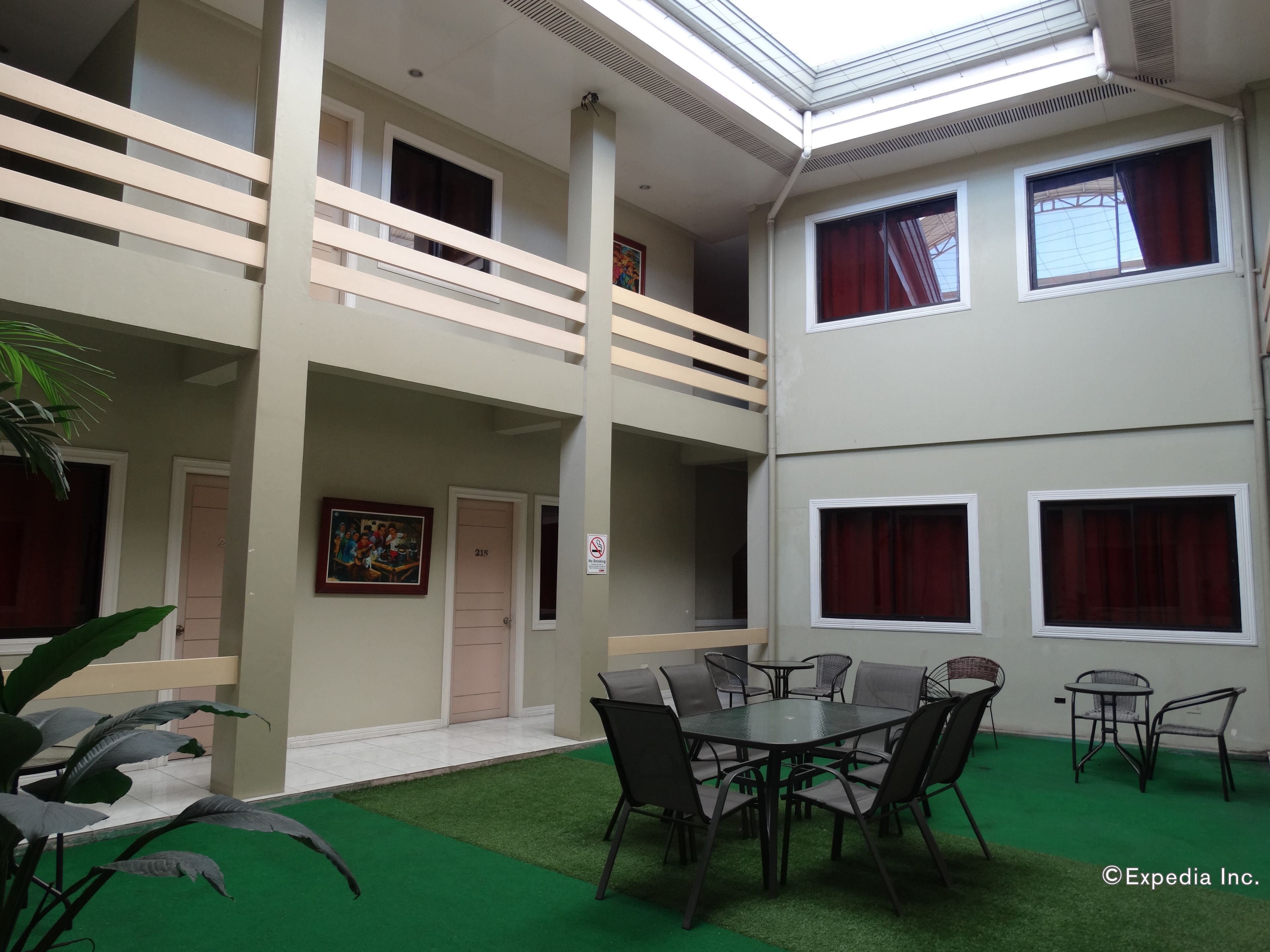 Interior de hotel de varios niveles con un atrio central, un comedor con mesas y sillas redondas, y un balcón con barandillas.