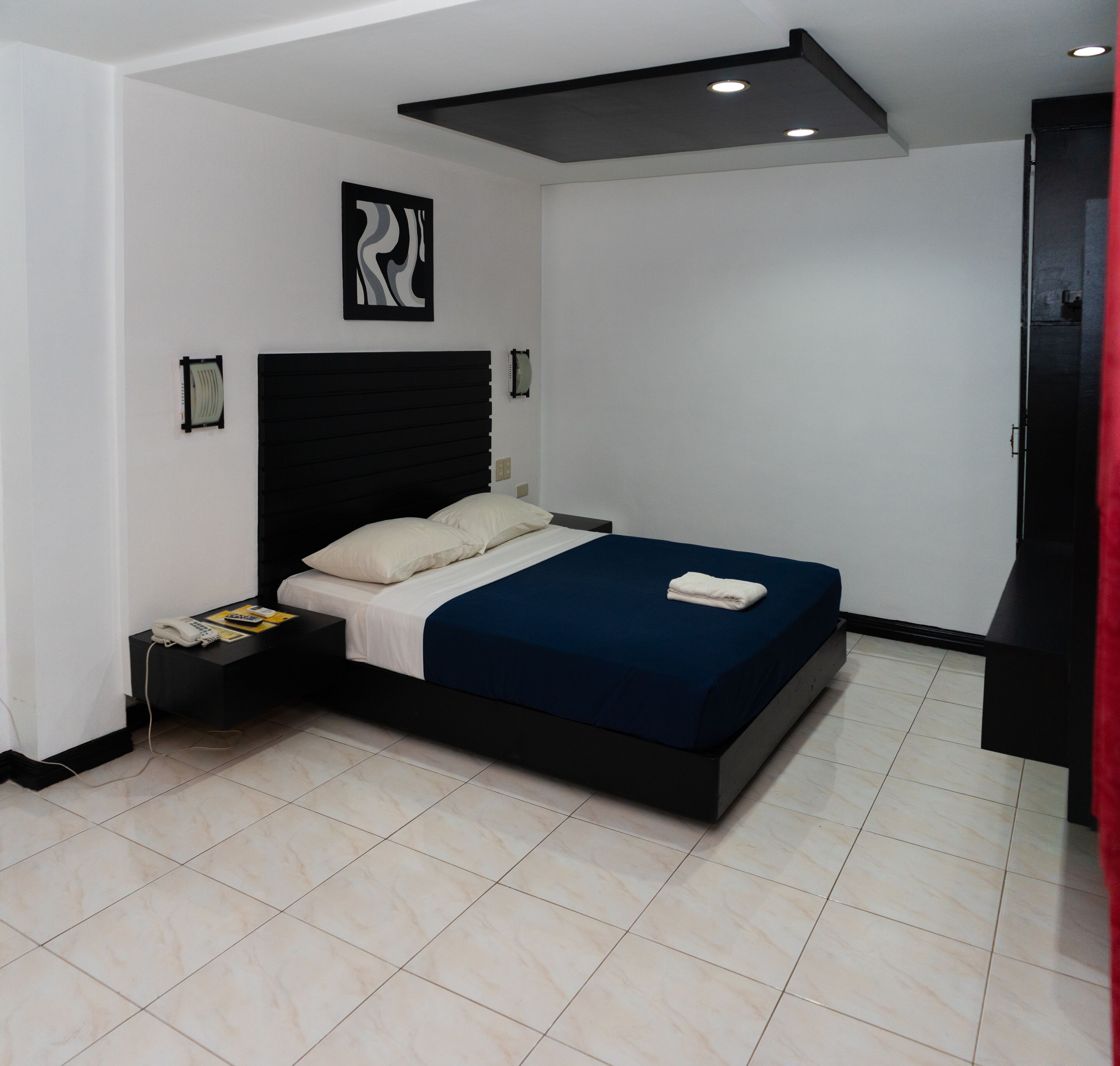 Un dormitorio moderno con una cama grande, una mesita de noche con un teléfono, y una lámpara en el techo.