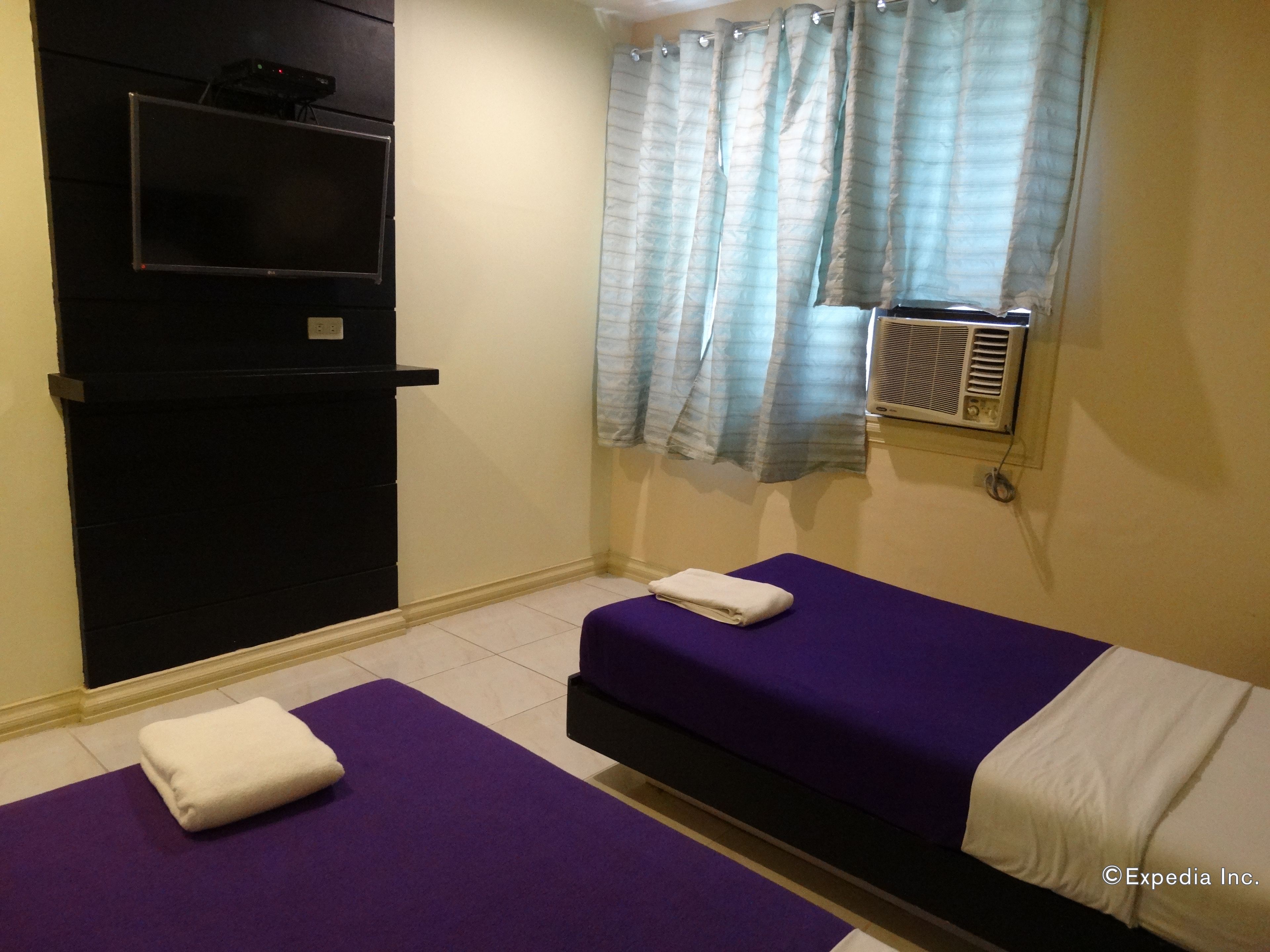 Une chambre d’hôtel avec deux lits, une télévision, un appareil de climatisation et une fenêtre avec des rideaux.