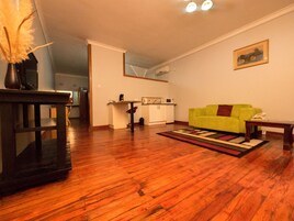 Una sala de estar con piso de madera, un sofá verde, una mesita y una cocina al fondo.