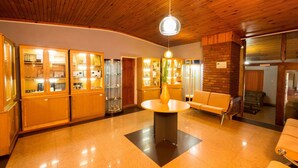 A lobby with wooden panel ceilings, a central round table with a vase, and glass display cabinets on the left. - Palmwood Lodge (Lusaka)