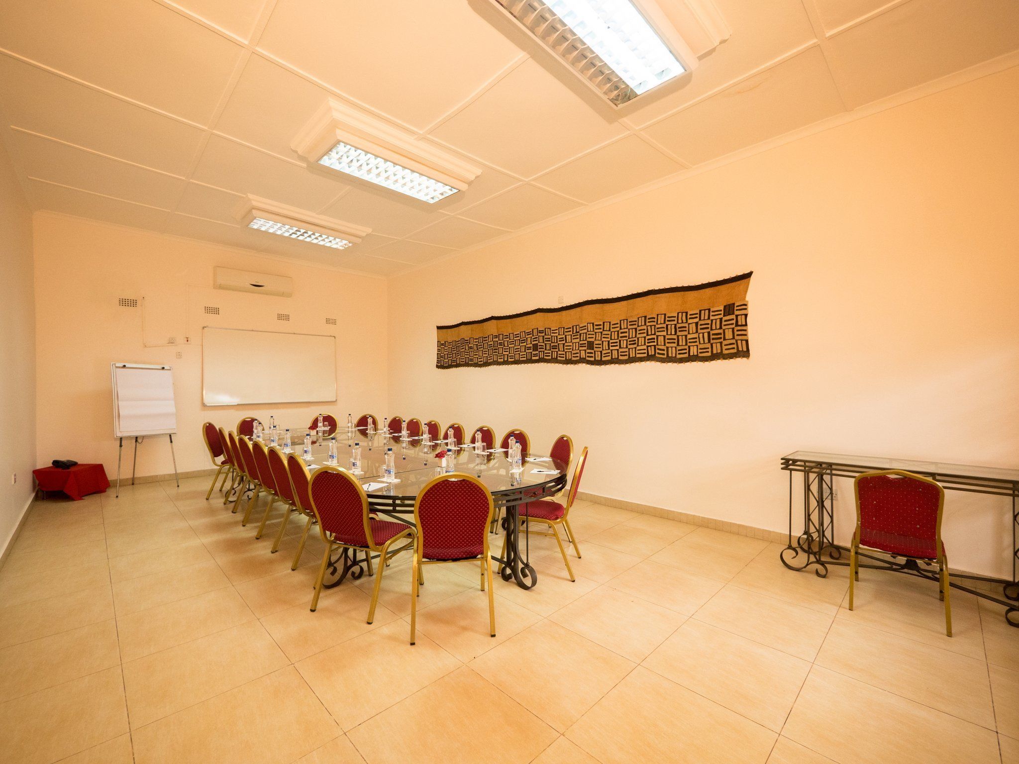 A conference room with a long table, red chairs, a whiteboard, and a patterned tapestry on the wall.