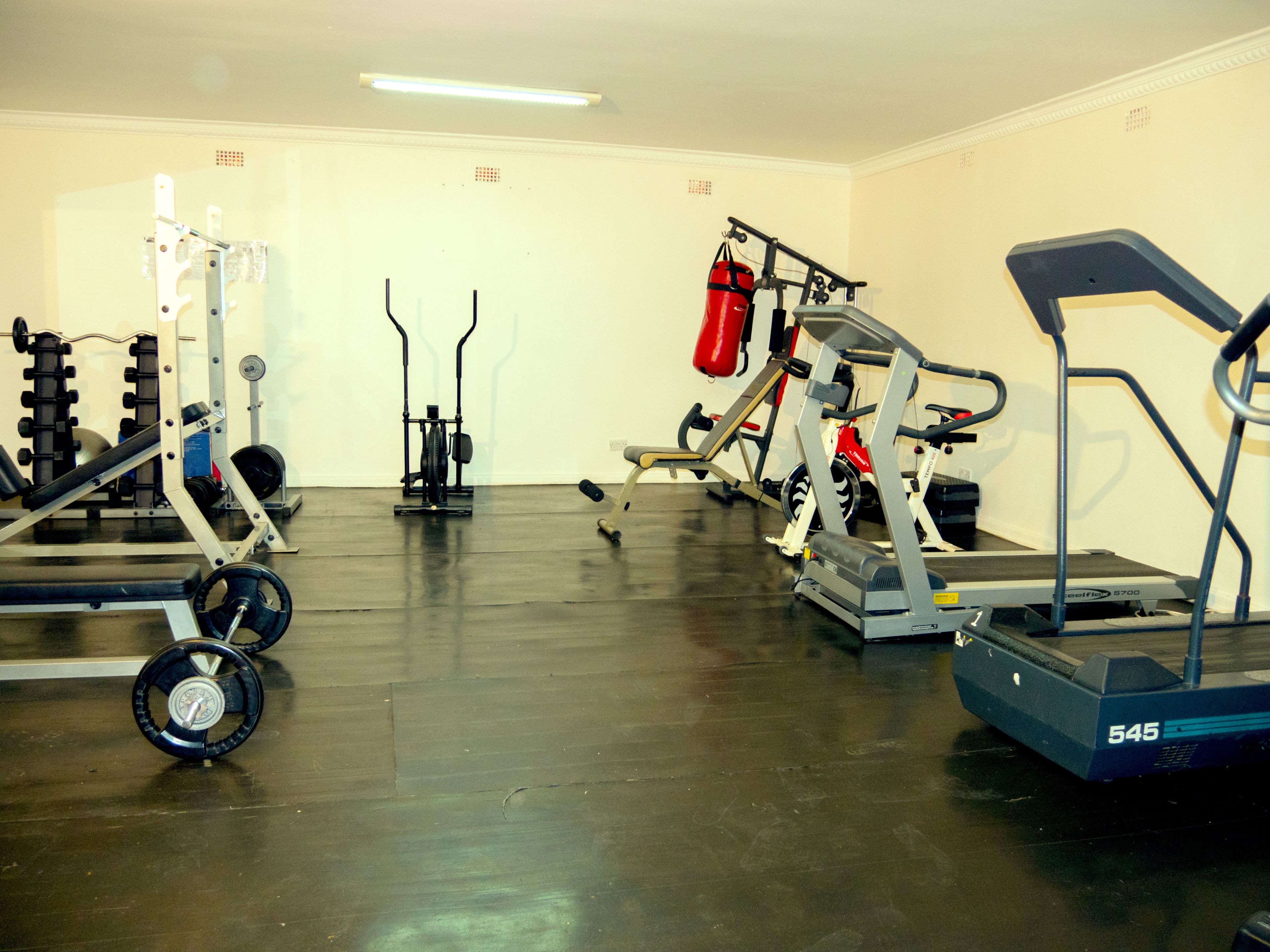 A gym with various exercise equipment including a treadmill, weight machines, and a bench.