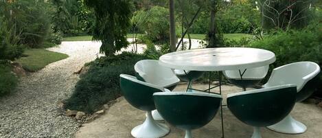 An outdoor garden patio with a round table and six green chairs.