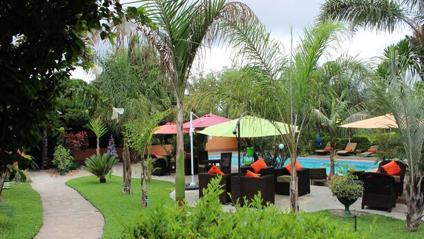 A poolside area with lounge chairs and umbrellas, surrounded by lush greenery and a stone pathway. - Palmwood Lodge (Lusaka)