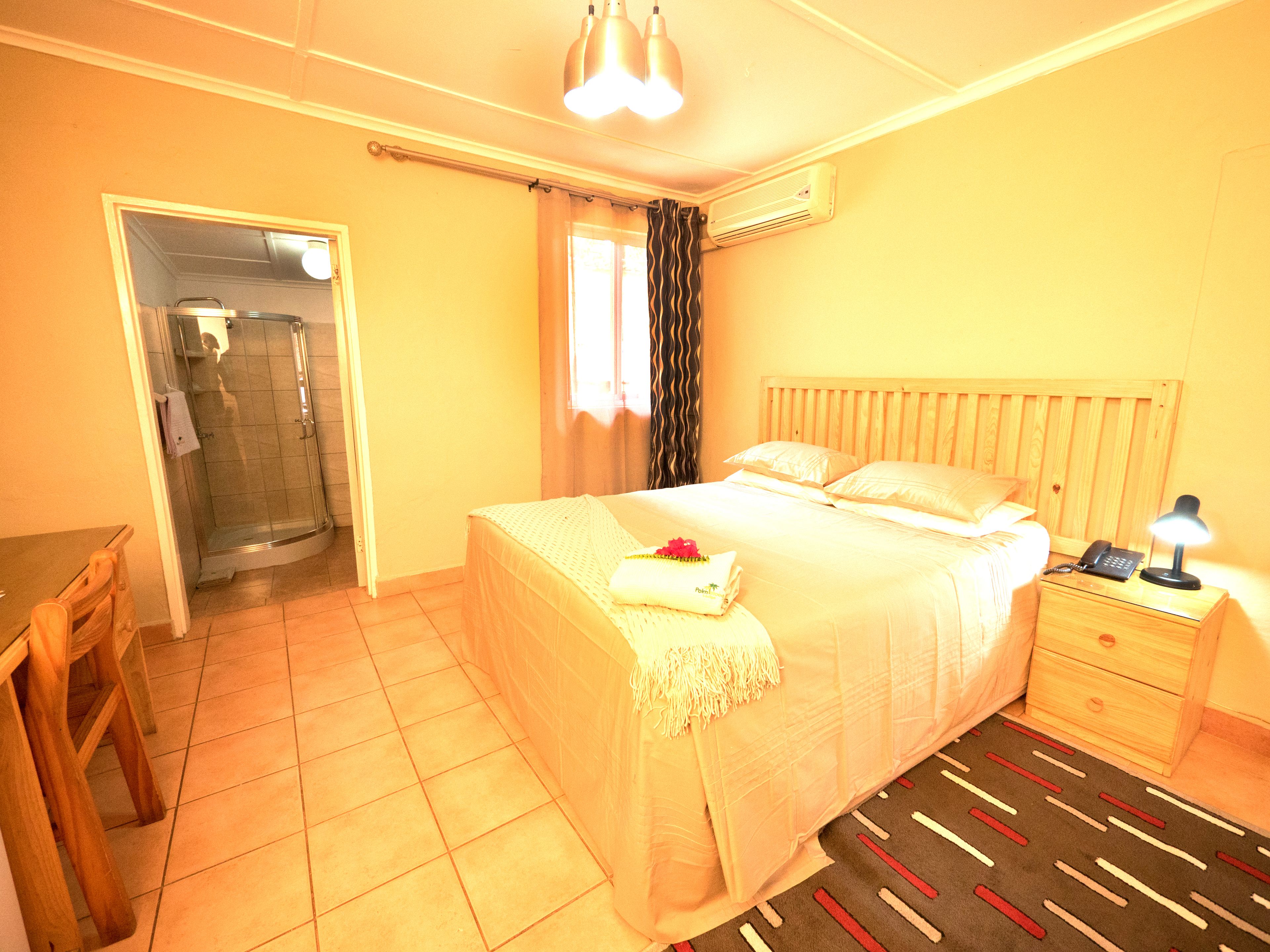 Une chambre d’hôtel comprenant un lit, une table de chevet, une commode et un espace douche.