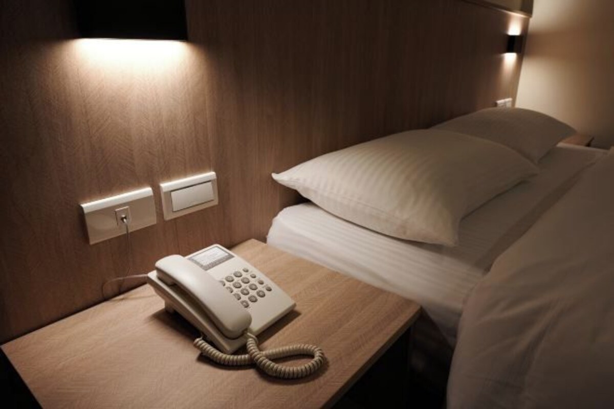 Une chambre d’hôtel équipée d’un téléphone sur la table de chevet, d’une prise électrique et d’une lampe fixée au mur.