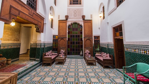 A traditional Moroccan interior with a tiled floor, wooden furniture, and ornate doorways.
