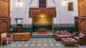 A traditional Moroccan interior with a tiled floor, wooden furniture, and a central seating area.