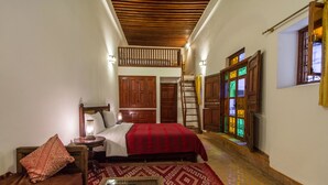 A bedroom with a bed, nightstand, lamp, and a wooden ladder leading to a balcony.