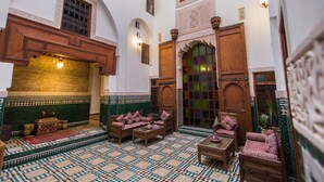 A traditional Moroccan interior with a tiled floor, wooden furniture, and ornate doors and windows.