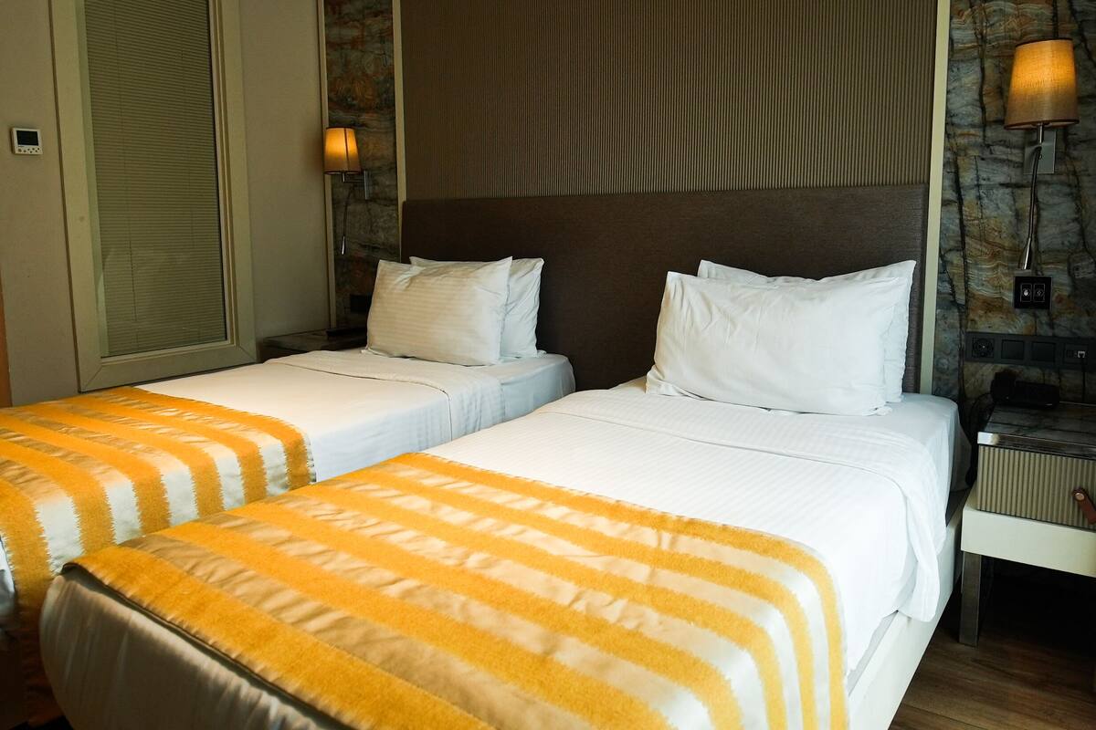 A hotel room with two beds, each with white bedding and striped blankets. There is a stone wall and a wooden headboard.