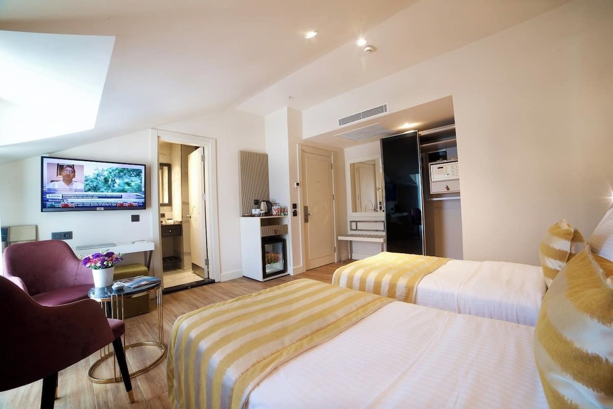 A hotel room with two beds, a desk, a chair, a TV, and a minibar.