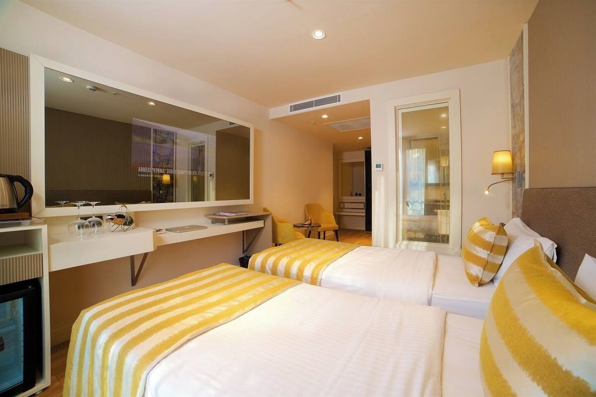 A hotel room with two beds, a desk, a chair, a TV, and a bathroom visible through an open door.