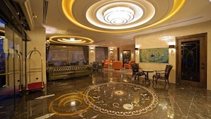 Een ruime lobby met een centrale zithoek, een grote kroonluchter en een decoratief vloerpatroon.