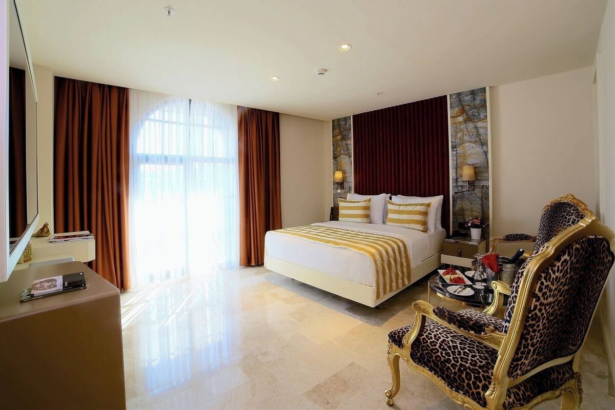A hotel room with a large bed, a desk, a chair, and a view of the outdoors.
