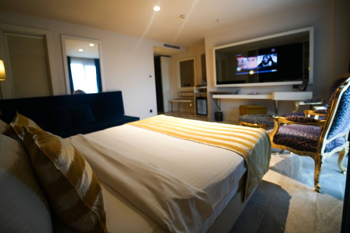 A hotel room with a large bed, a television, a sofa, and a chair.