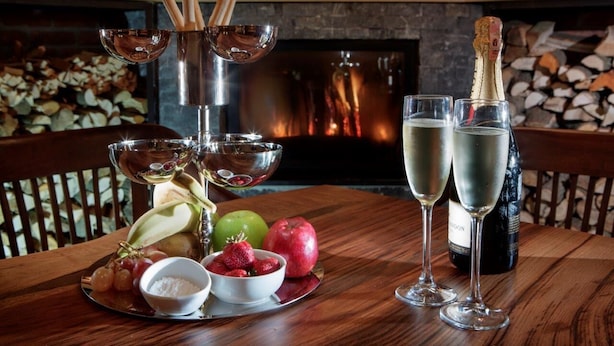 Een houten tafel met een fruitschaal, twee champagneglazen en een champagnefles.