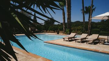 Una piscina al aire libre, sombrillas, sillones reclinables de piscina