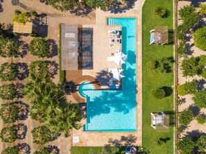 Vista aérea de un complejo turístico con piscina, tumbonas y palmeras.