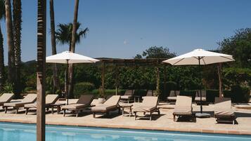 Una piscina al aire libre, sombrillas, sillones reclinables de piscina