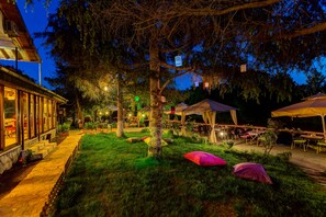 Un espace de restauration en plein air, avec des tables et des chaises, entouré d’arbres et bordé d’un bâtiment doté de grandes fenêtres.