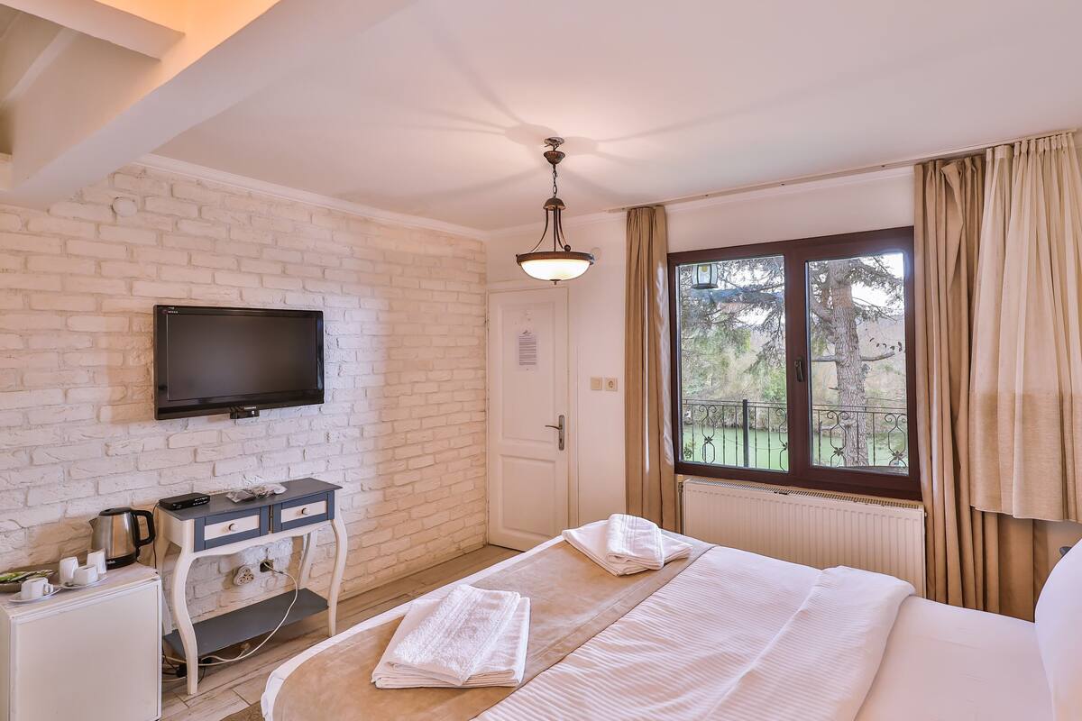 Une chambre d’hôtel avec un lit, un bureau doté d’une bouilloire, une télévision et une fenêtre avec des rideaux.