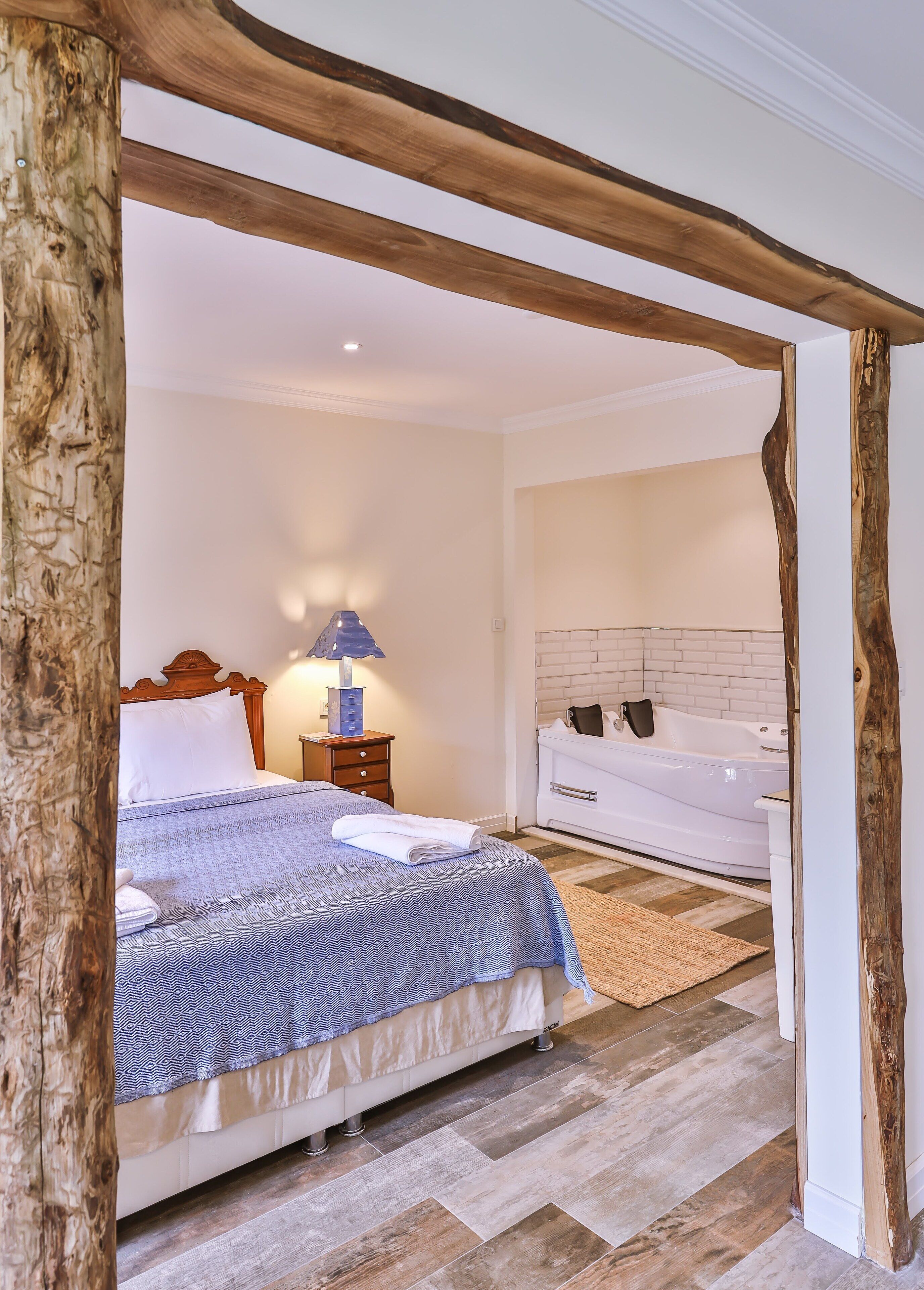 A bedroom with a bed, bedside table, lamp, and a bathroom with a bathtub.