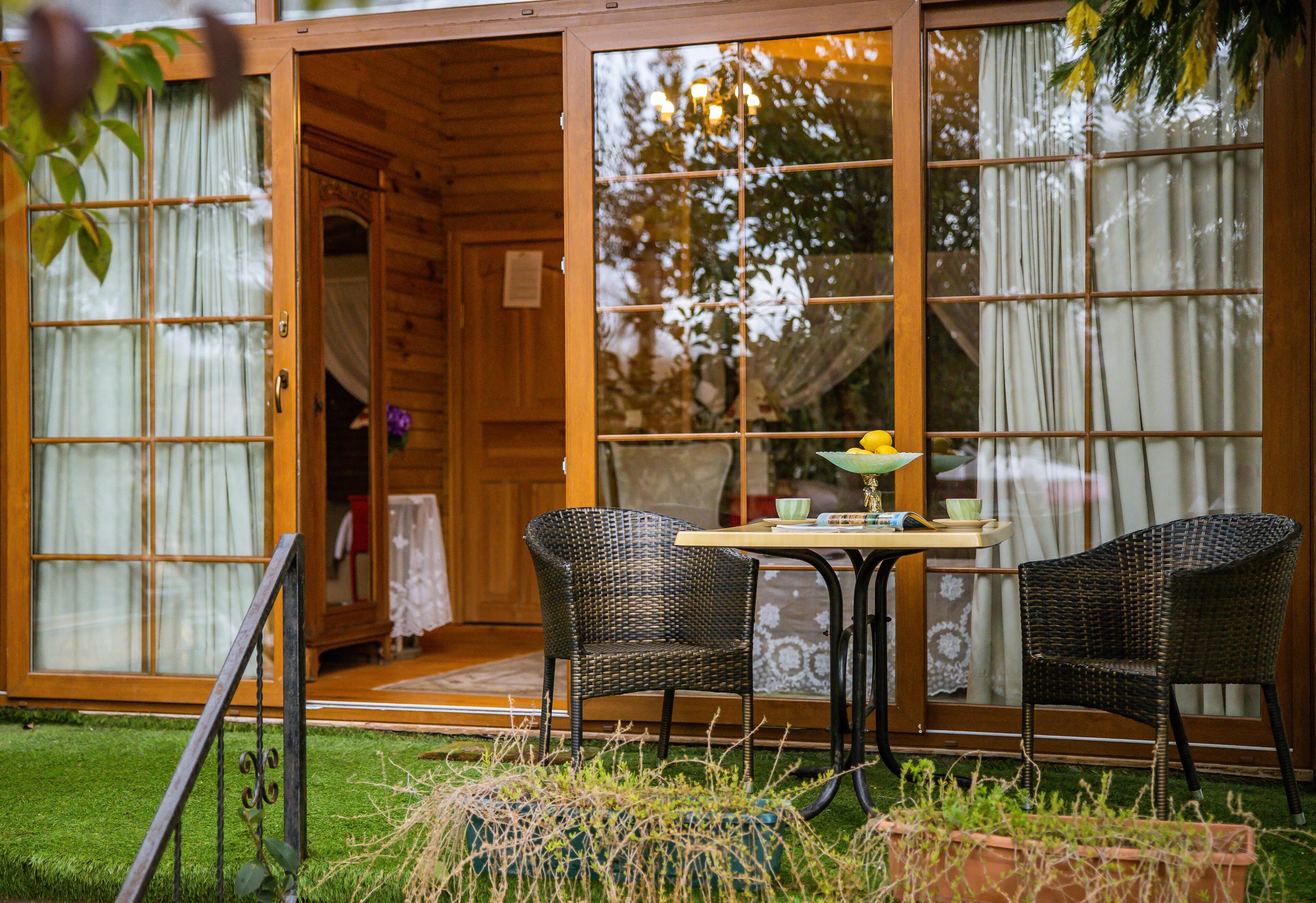Una cabaña de madera con puertas correderas de vidrio, una mesa de comedor con sillas y un pequeño jardín.