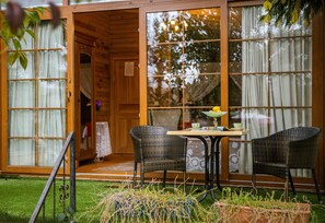 Une cabane en bois dotée de portes coulissantes en verre, d’une table à manger avec des chaises et d’un petit espace jardin.